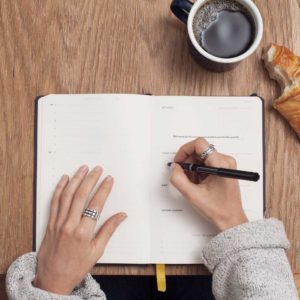 female hands about to write in a journal with a cup of coffee nearby