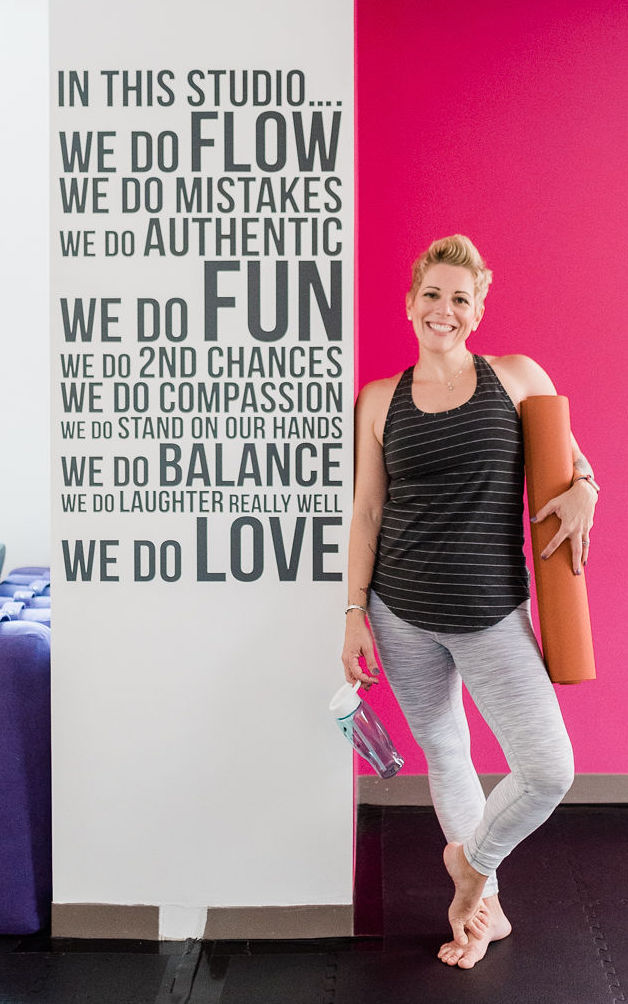 Gretchen Schock standing next to a wall in the Bee Yoga Fusion studio holding a yoga mat