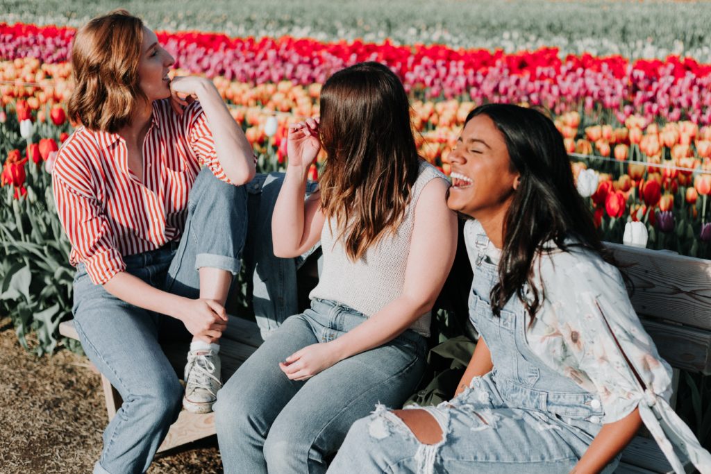 three girls laughing together with flowers behind them