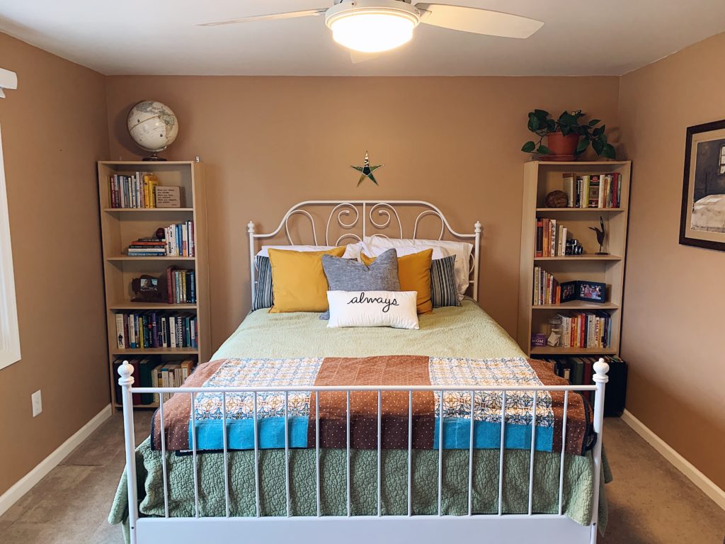 Guest bedroom with bookshelves on either side of the bed that are clear of clutter. Bed has pillows and quilts. Very welcoming space.