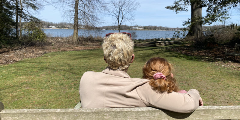 a woman and a preteen girl siting on a bench looking out at the water