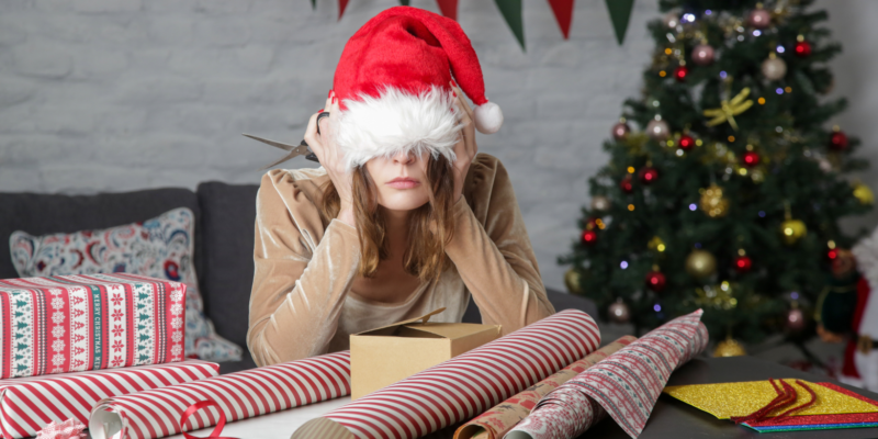 woman with santa hat pulled over her eyes with wrapping paper and a christmas tree behind her