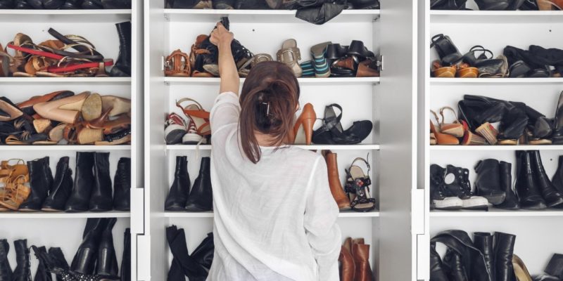 woman standing at a large closet of only shoes and choosing one pair