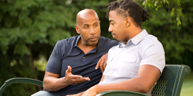 Older black male giving advice to younger black male in a park setting