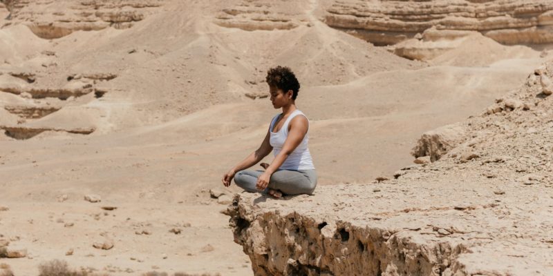 woman sitting on the edge of the cliff in half lotus pose meditating