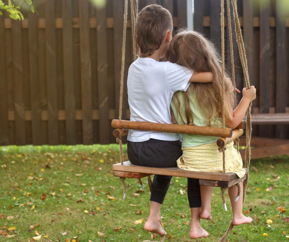 an older brother hugging younger sister while on a swing.