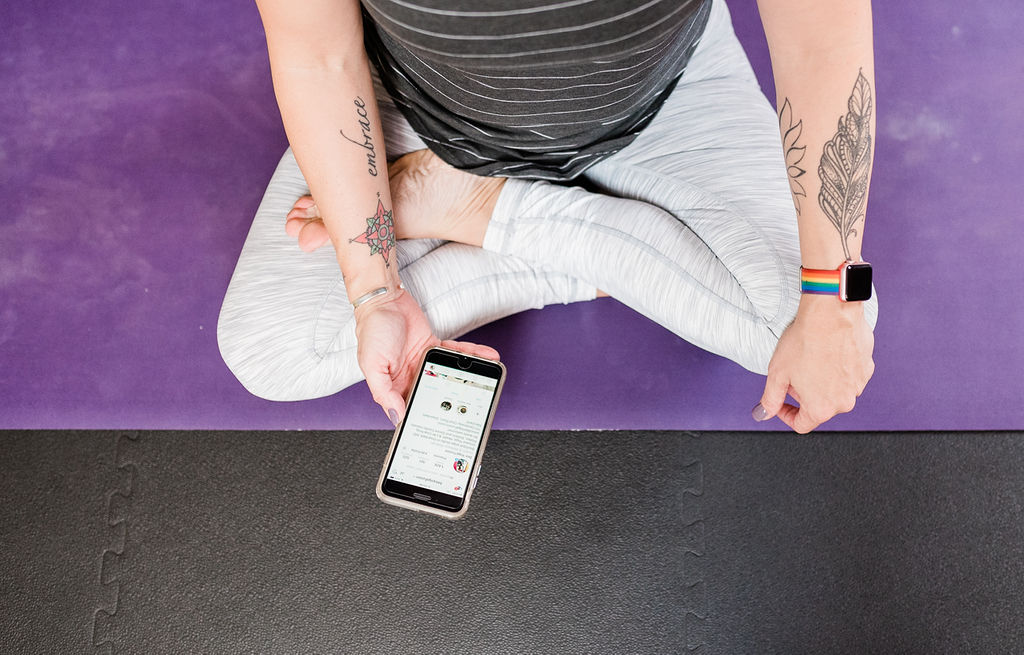 Gretchen Schock sitting in half lotus pose holding her phone looking at an instagram page